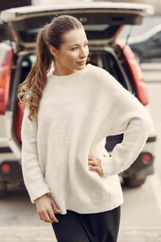 Woman in a white sweater. Girl in a spring city. Lady by the car.