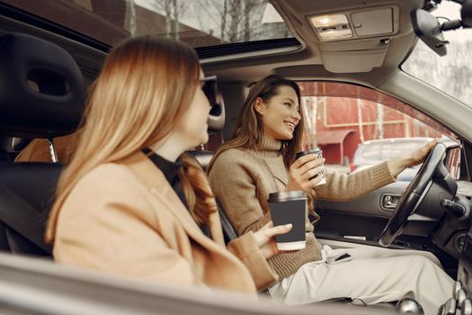 Girls inside the car. Women with a coffee. Friends have fun in a car.