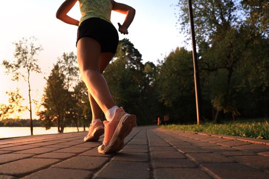 Runner feet running on road closeup on shoe, outdoor at sunset or sunrise