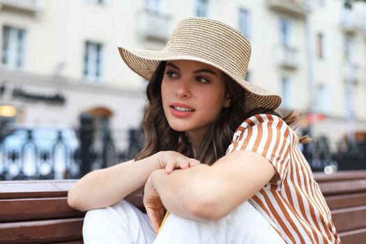 Beautiful smiling young brunette woman sitting on bench in park