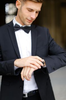 Young handsome man wearing black suit and waiting, loking at watch. Concept of male model and businessman.