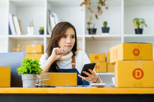 Work from home. happy women selling products online Start a small business owner by using smartphone and laptop computer to calculate prices and prepare for postage