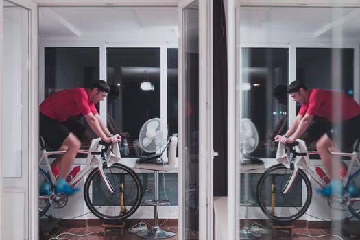 Man cycling on the machine trainer he is exercising in the home at night. Playing online bike racing game during coronavirus covid19 lockdown. New normal concept.