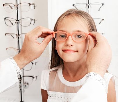 Beautiful little girl choosing glasses at clinic