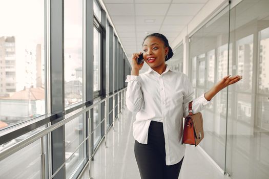 Black girl in the office. Woman in a white shirt. Lady use the phone.