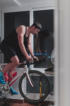 Man cycling on the machine trainer he is exercising in the home at night. Playing online bike racing game during coronavirus covid19 lockdown. New normal concept.