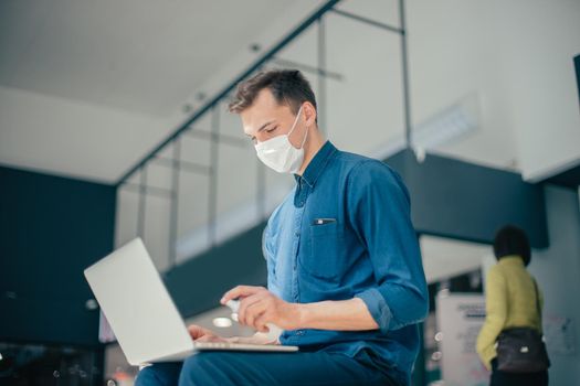 young casual man in protective mask disinfecting his laptop. pandemic in the city