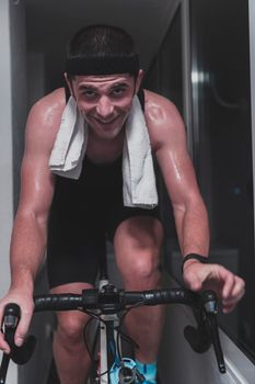 Man cycling on the machine trainer he is exercising in the home at night. Playing online bike racing game during coronavirus covid19 lockdown. New normal concept.