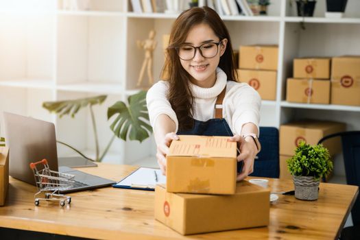 Business owner picking up parcel boxes And use a computer to check online orders to prepare the packaging. pack products to send to customers