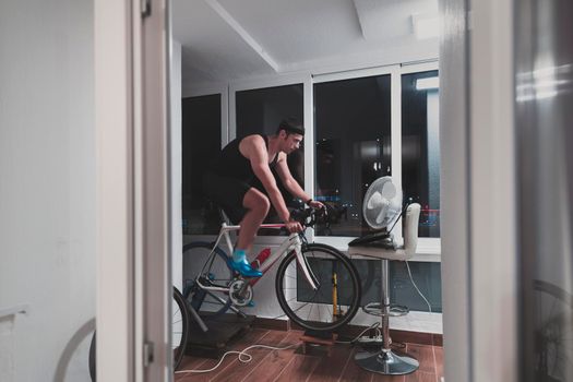 Man cycling on the machine trainer he is exercising in the home at night. Playing online bike racing game during coronavirus covid19 lockdown. New normal concept.