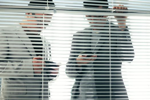 through the blinds. business colleagues reading messages on their smartphones.