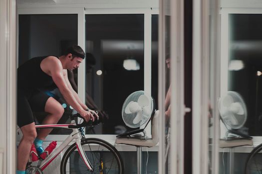 Man cycling on the machine trainer he is exercising in the home at night. Playing online bike racing game during coronavirus covid19 lockdown. New normal concept.