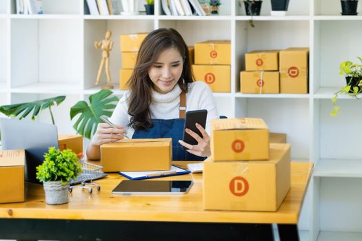 Work from home. happy women selling products online Start a small business owner by using smartphone and laptop computer to calculate prices and prepare for postage