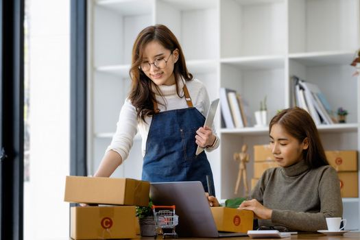 Two happy women selling products online. Start a small business owner with a pen to write down the addresses of customers and prepare them for postage