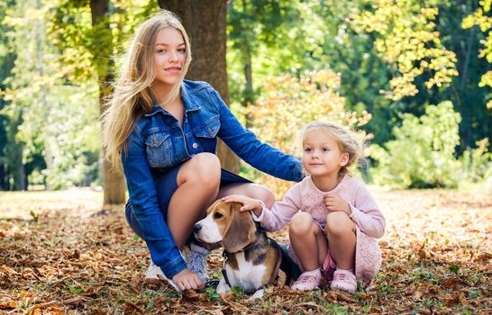 Happy sisters playing with dog in autumn park