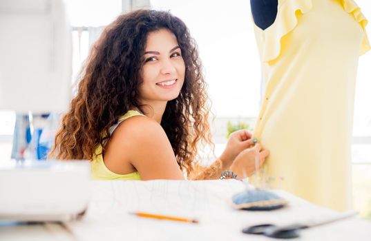 Smiling tailor pinning parts of dress in workshop