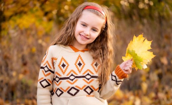 Nice little girl holding autumn leaves outdoors