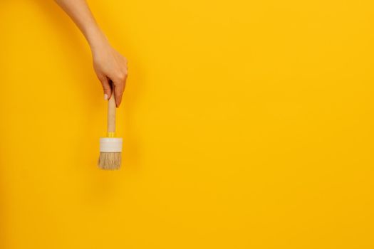Woman hand holding wooden paint brush on yellow background with copy space. Concept of creativity and hobbies. Working tool for home design project