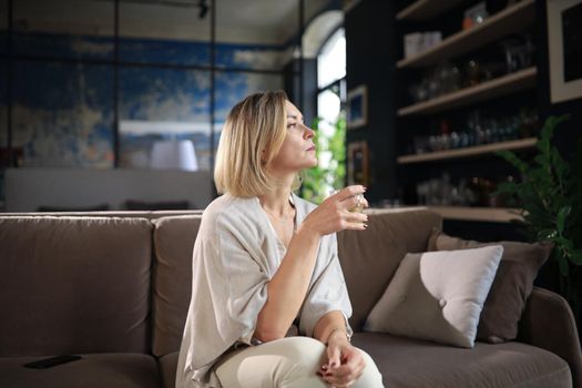 Happy mature woman resting on comfortable sofa drink coffee or tea, looking away, relaxing on cozy couch at home enjoy hot beverage