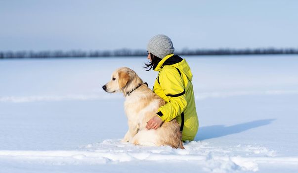 Rear view of friendly dog and woman sitting on snowy field