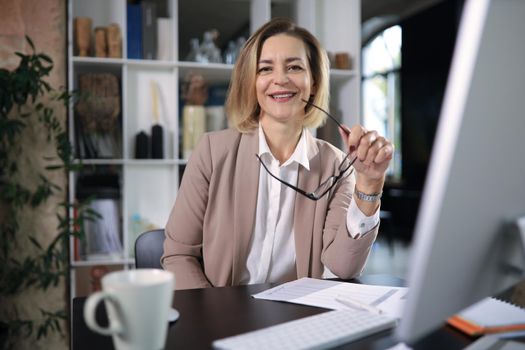 Attractive middle aged woman working at office, using contemporary desktop computer