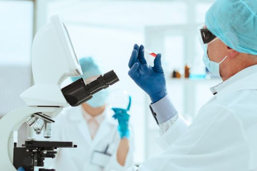 close up. scientist in protective gloves holds an ampoule with a new drug.