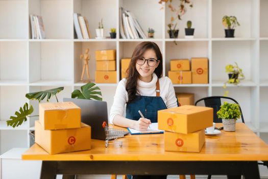 Entrepreneur owner using pen point note and laptop checking online purchase shopping order to preparing pack product box. Packing goods for delivery to customer