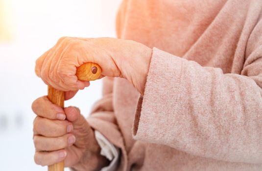 hands of old woman holding cane in room