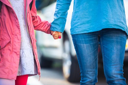 Little girl holding mother's hand on car background, close up
