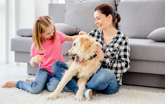Pretty mother and cute daughter playing with adorable dog at home