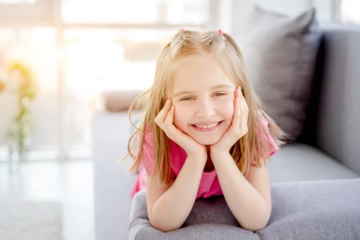 Happy little girl resting on sofa with head on hands indoors