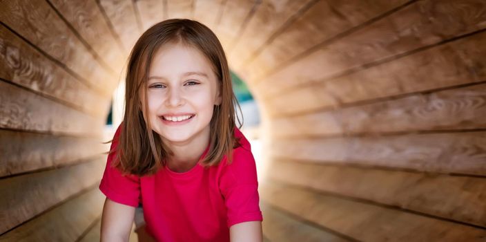 Smiling little girl sitting in wooden pipe, panoramic orientation