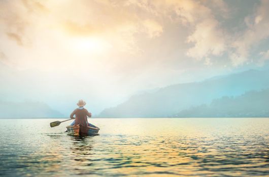 Back view of lonely fisherman in boat on morning lake