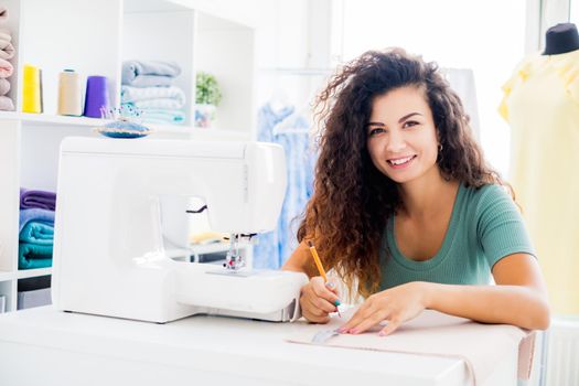 Happy tailor measuring cloth in light workroom