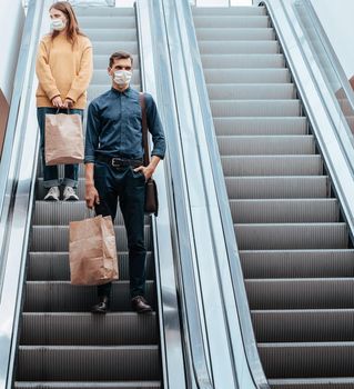 young man in a protective mask standing on an escalator in a shopping center. coronavirus in the city