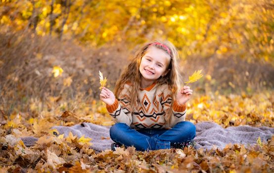 Cute little girl holding yellow leaves outdoors