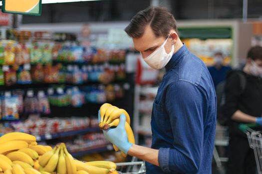 customer in protective gloves choosing bananas in a supermarket. hygiene and health care