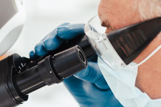 close up. scientist biologist in a protective mask looking through a microscope. science and health protection.