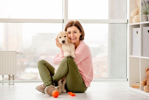 Happy woman cuddling cute puppy at home