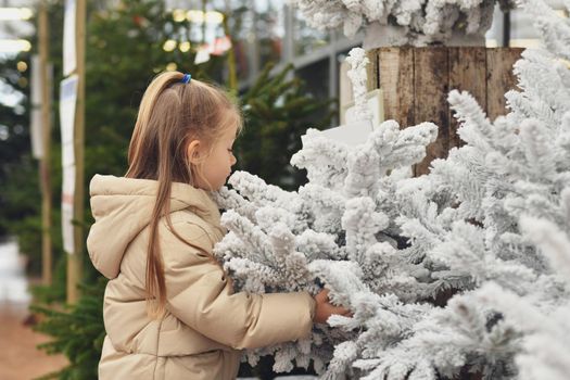 A girl and a white christmas artificial trees for sale on a shop