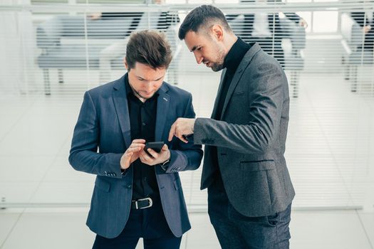 colleagues with a smartphone standing in the office lobby. photo with a copy-space.