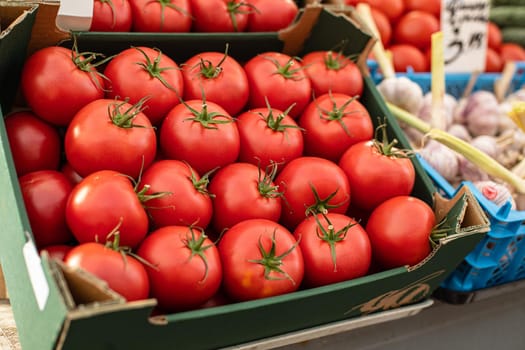 Close up of box with bright red tomatoes ready for sale at farmers market next to other vegetables. Market and trade concept