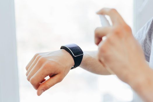 close up. young man is spraying alcohol antiseptic on his smart watch.