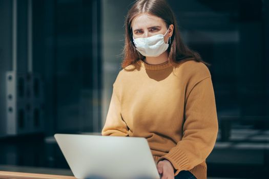young woman works on a laptop during a pandemic. people and technology