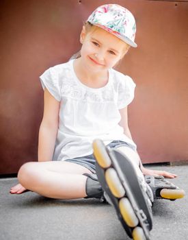 Beautiful little girl on roller skates sitting in park