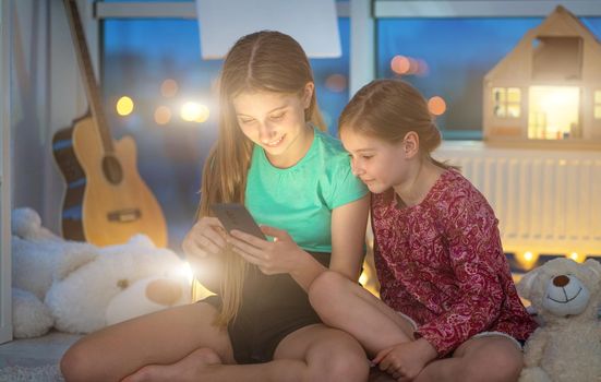Sisters using smart phone at home in evening