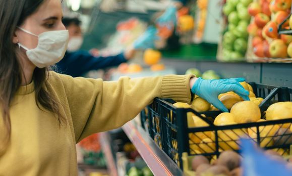 young woman in a protective mask choosing lemons in a store. coronavirus in the city