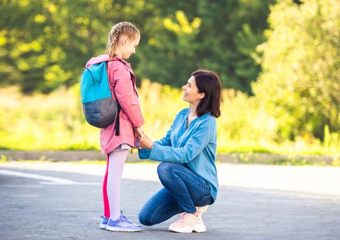 Schoolgirl with backpack saying goodbye to mother before class on parking