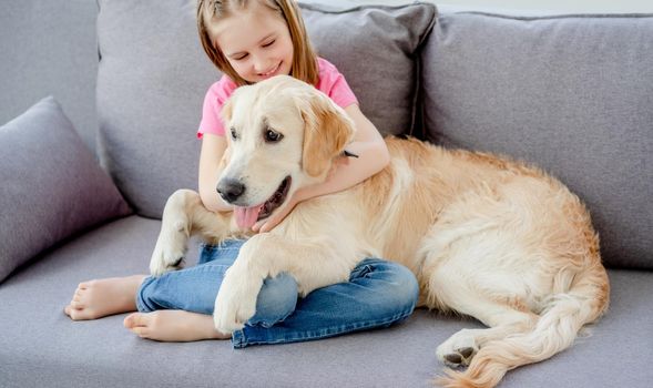 Happy little girl on sofa with golden retriever in light room