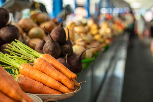 Close-up focused view over organic raw carrots and beetroots sorted in different plates on the counter. Blurred vegetables in the background. Local market.